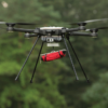 The SkyRanger R70 carrying a red bag while flying in front of trees