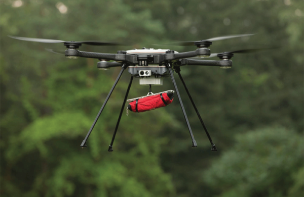 The SkyRanger R70 carrying a red bag while flying in front of trees