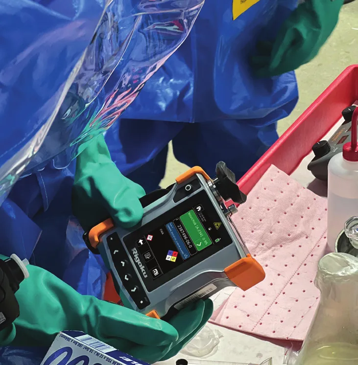 Operator in a blue suit scanning a sample with the CQL Max-ID inside a plastic enclosure