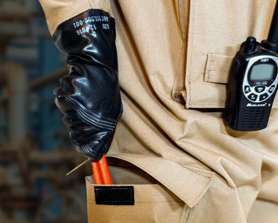 Gloved hand of a DuraChem 500 wearer reaching into a thigh pocket, with a two-way radio clipped to the suit