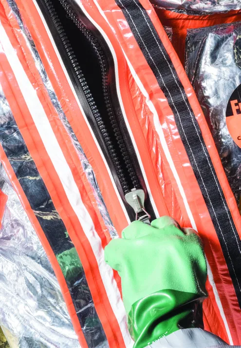 Gloved hand closing the black AquaSeal gas-tight zipper between orange-taped storm flaps