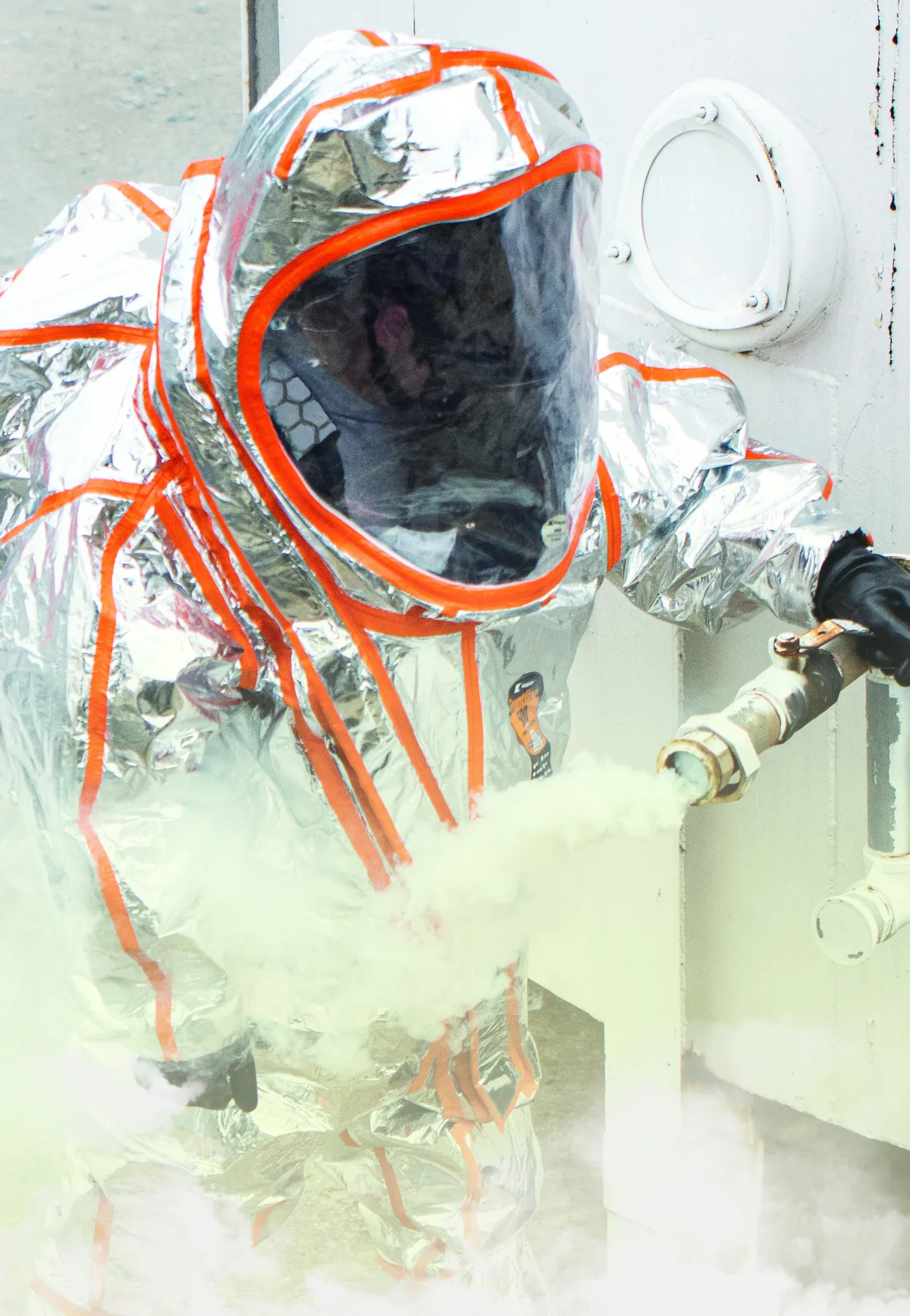 Responder in a silver Kappler Frontline 500 vapor suit with orange seam tape closing a leaking valve in a cloud of vapor